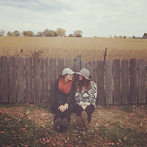 two women leaning on brown wooden fences thumbnail