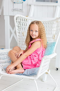 girl in pink sleeveless dress sitting on white wicker armchair thumbnail