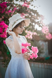 Woman Wearing Sun Hat and White Dress Holding Pink Bougainvilleas thumbnail