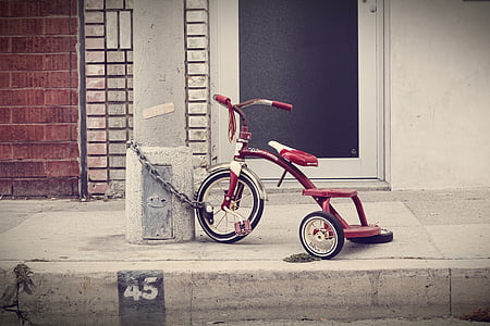 red and white bicycle chained on white post near black and white wooden closed door thumbnail