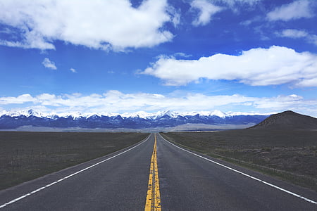clear road in between field under white clouds and blue sky thumbnail