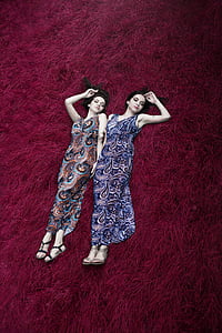 two women wearing multicolored paisley-print dresses lying on red surface thumbnail
