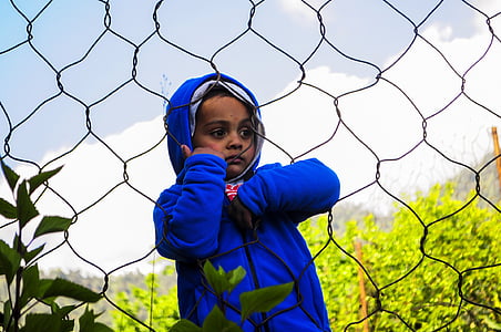 boy wearing blue hoodie holding on link fence thumbnail