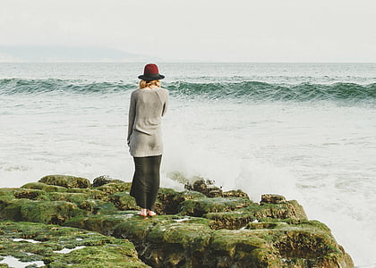 woman standing on green rocky hill near ocean thumbnail