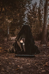 person in black cloak holding knife in forest thumbnail