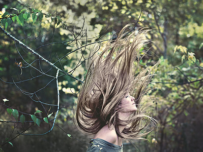 woman with blonde long hair flipping her hair near trees thumbnail
