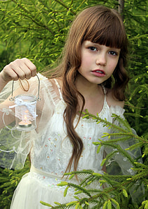 girl wearing white floral spaghetti-strap tutu dress holding clear glass candle lantern beside green leaf plants thumbnail