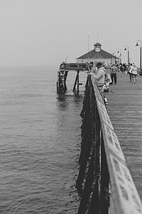 grayscale photo of people on dock fishing during daytime thumbnail