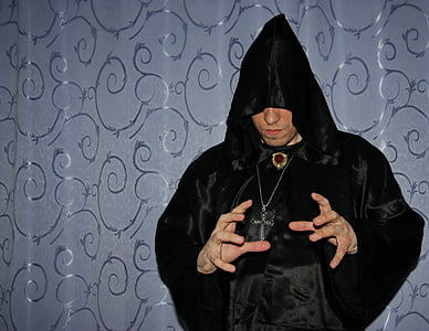 person wearing black robe and silver-colored crucifix necklace using hand gesture thumbnail