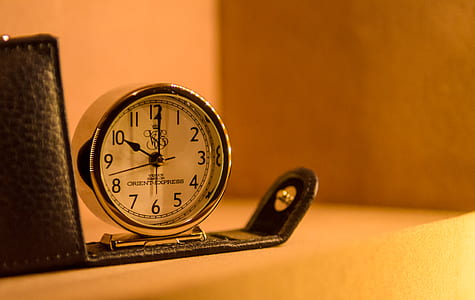 round silver alarm clock beside black leather case thumbnail