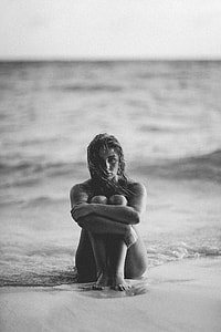 grayscale photo of  female sitting on sand beside seashore thumbnail