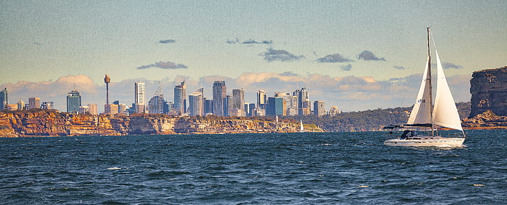 White Sail Boat Sailing on Body of Water Near City Buildings thumbnail