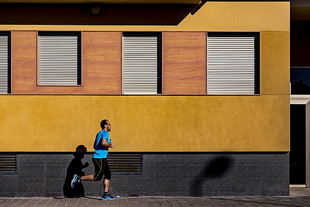 man runs on gray concrete pathway beside yellow building thumbnail