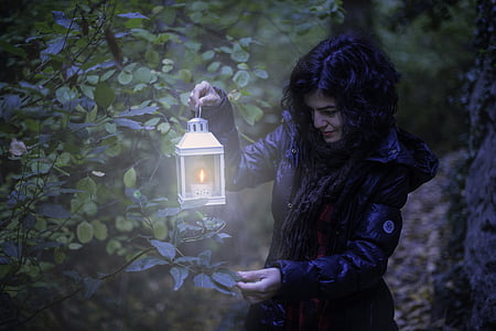 woman wearing black zip-up hooded jacket holding white candle lantern thumbnail