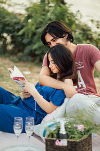 woman reading book while lying on mans lap sitting on brown textile thumbnail