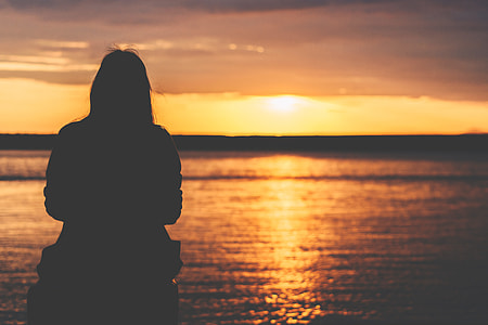 silhouette of person sitting facing towards body of water during golden time thumbnail