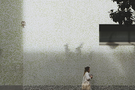 woman in white long-sleeved shirt walking beside white and green wall during daytime thumbnail