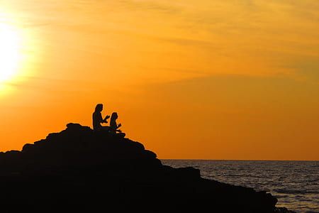 silhouette photo of two people sitting on rock facing body of water thumbnail
