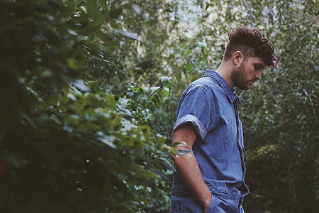 man in blue denim collared shirt standing between plants at daytime thumbnail