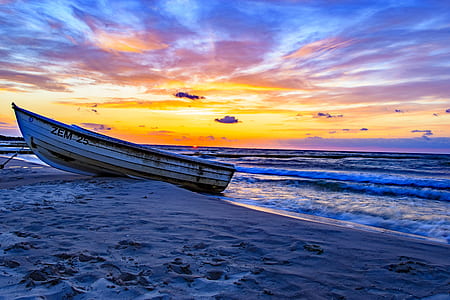 white and yellow boat dock on sand near wavy ocean under orange sky during golden hour thumbnail