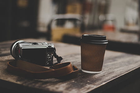 gray point-and-shoot camera beside black cup on brown wooden table thumbnail