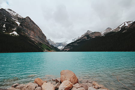 body of water near mountain covered by snow under white clouds at daytime thumbnail