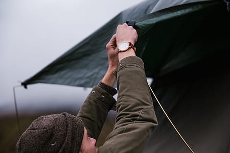 A young caucasian man wearing brown jacket setting up tent thumbnail