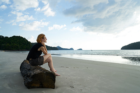 woman wearing black shirt with gray short sitting on brown slab near the body of water during daytime thumbnail