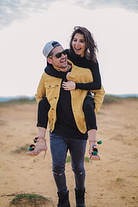 man carrying woman on back while walking on sand thumbnail