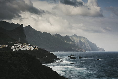 wide angle photo of mountain near body of water under cloudy sky thumbnail