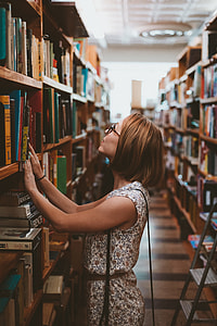 woman wearing white and brown floral dress standing near bookshelf looking up thumbnail