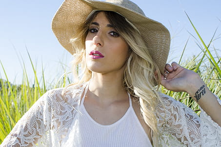 Woman Wearing Brown Hat and White Cardigan Standing in Middle of Grass Field thumbnail
