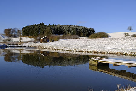 brown house near body of water and trees under blue sky during daytime thumbnail