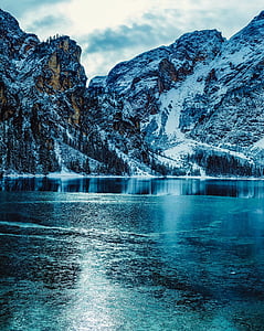 calm body of water near mountain covered by snow under white cloudy sky at daytime thumbnail