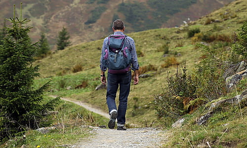 man in blue long-sleeved top and black pants with backpack walking during daytime thumbnail