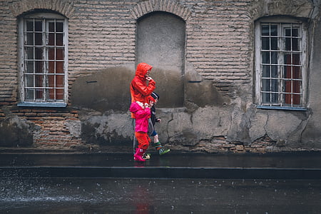 person wearing red rainy coat while with his/her children walking on black asphalt road thumbnail