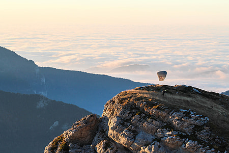 hand glider on top of rock formations near silhouette of mountains under cloud sky thumbnail
