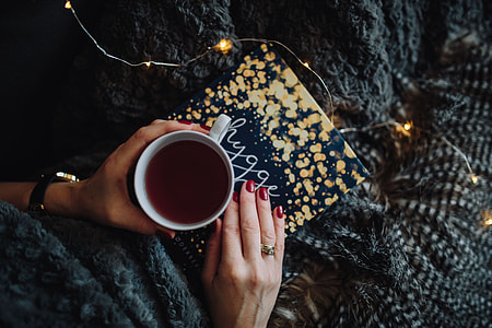 Young woman at home reading Hygge book and drinking thumbnail