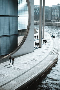 nine people walking beside high-rise building near body of water at daytime thumbnail