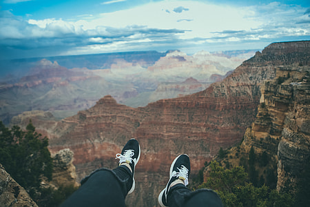 person wearing black shoes on hill over-viewing red and black mountains thumbnail