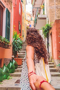 woman holding hand while walking on gray pavement staircase alley beside buildings at daytime thumbnail