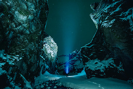 person standing in between rock formation during nighttime while holding blue light thumbnail