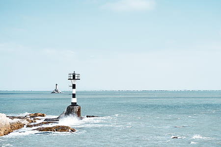 white and black lighthouse between rock and sea at daytime thumbnail