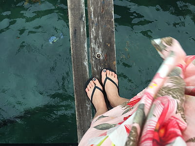 person wearing pair of black flip-flips standing on wood plank over water thumbnail