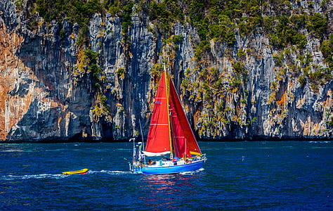 blue and white sailing boat near cliff thumbnail