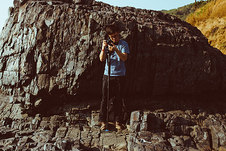 man standing beside rock formation holding DSLR camera during daytime thumbnail