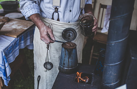 person in blue long-sleeved shirt standing while working behind brown and white wooden table and near brown wooden armless chair thumbnail