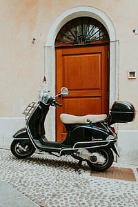 black and white motor scooter in front of brown wooden door thumbnail