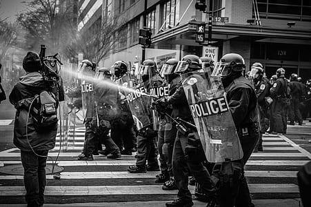 grayscale photography of police with shields stands on pedestrian lane thumbnail