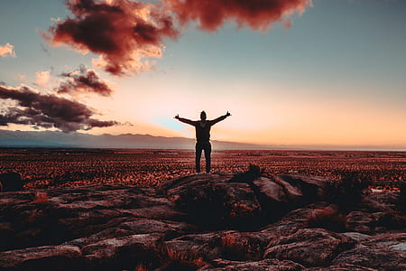 man spreading hands while standing on rock thumbnail